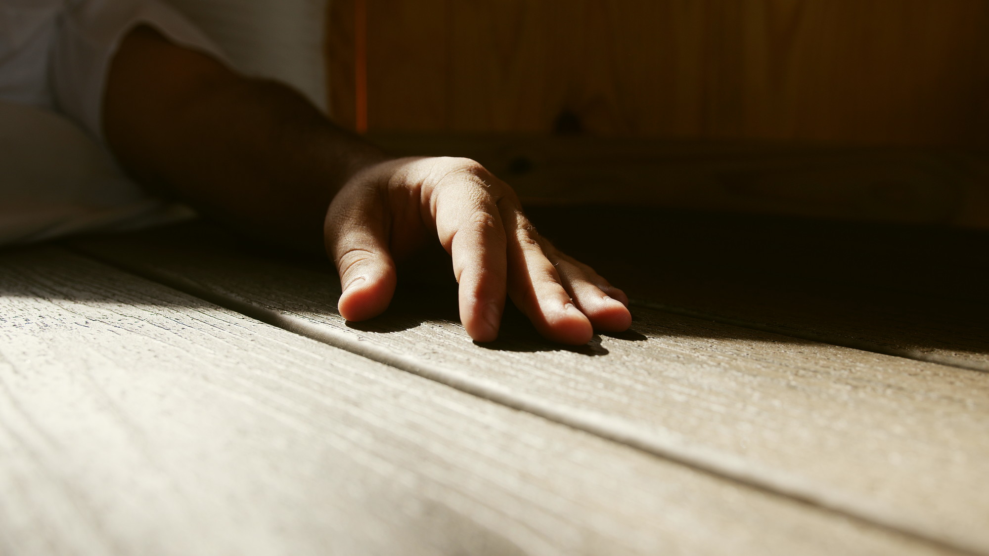 A hand resting in a band of sunlight across a wooden floor.